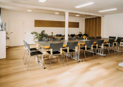 Ein helles Besprechungszimmer mit mehreren Tischen und Stühlen, Blumen in Vasen auf den Tischen, ein großes Fenster auf der linken Seite.