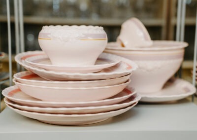 Eine Reihe von rosa Porzellantellern und einer Schüssel auf einem Regal, die gepflegte Kanten und dekorative Details aufweisen.