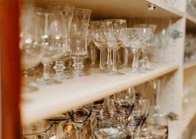 Eine Sammlung von Gläsern in einem schlichten Regal; verschiedene Formen und Höhen sind deutlich erkennbar, und einige Gläser reflektieren das Licht.