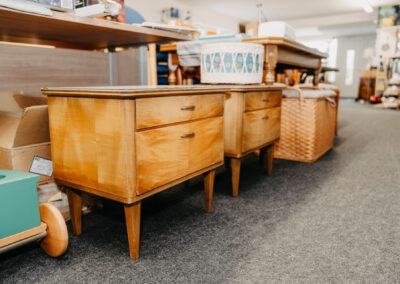 Zwei vintage Holznachttische stehen nebeneinander auf einem grauen Teppich im Raum, umgeben von weiteren Gegenständen und Möbeln.