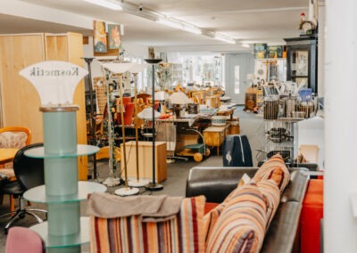 Ein gut sortierter Second-Hand-Laden mit verschiedenen Möbelstücken, darunter Lampen und Tische. Die Produkte sind ordentlich angeordnet und vielfältig in der Farben- und Formenvielfalt.