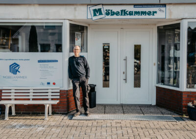 Ein Mann steht vor dem Geschäft ''Möbelkammer'' in Lohne. Das Geschäft bietet eine nachhaltige Möbelauswahl und Jugendförderprojekte an.