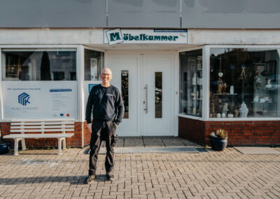 Ein Mann steht vor dem Geschäft "Möbelkammer" in Lohne, lächelt freundlich und trägt einen schwarzen Pullover mit dem Namen "Günter".