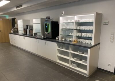 Moderne Küchenausstattung mit Geschirr, Gläsern, Kaffeemaschine und Wasserspender in einem Raum.