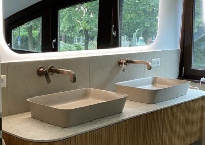 Moderne Badezimmeransicht mit zwei ovalen Waschbecken aus Keramik auf einer eleganten Holzablage. Eine große Spiegelfläche reflektiert die Umgebung.