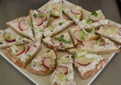 Verschiedene belegte Brote auf einem weißen Teller, angerichtet mit Radieschen und Frühlingszwiebeln; das gesamte Arrangement wirkt appetitlich und frisch.