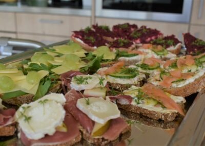 Ein Tablett mit verschiedenen belegten Broten, darunter Käse, Schinken, Lachs und Trauben. Die Böden sind rustikal und mit frischen Kräutern garniert.