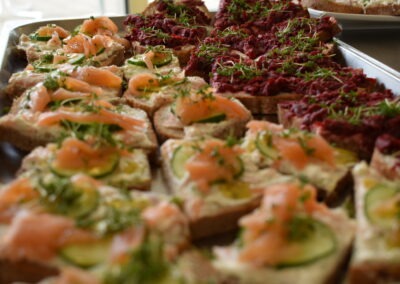 Ein platter mit belegten Broten; einige sind mit Räucherlachs, Gurkenscheiben und frischen Kräutern belegt, während andere mit einer roten Aufstrichvariante dekoriert sind.