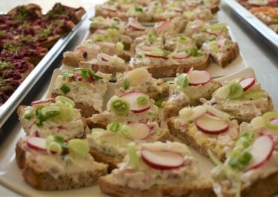 Mehrere belegte Brotscheiben mit einer cremigen Aufstrichmischung, belegt mit Radieschen und Frühlingszwiebeln, auf einem weißen Teller arrangiert.