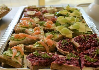 Eine Platte mit verschiedenen belegten Broten, darunter Lachs, Gurken und Rote-Beete-Aufstrich, sorgfältig angerichtet für eine Präsentation.