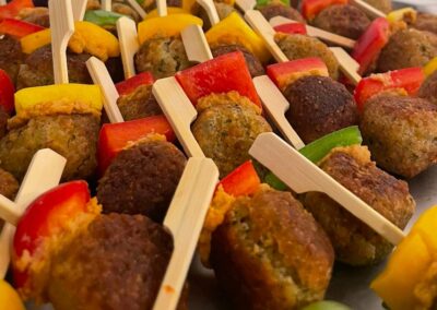 Verschiedene Spieße mit Gemüse und knusprigen Fleischbällchen in einer Anordnung auf einem Tisch; die bunten Zutaten sind auf holzähnlichen Stäbchen aufgesteckt.