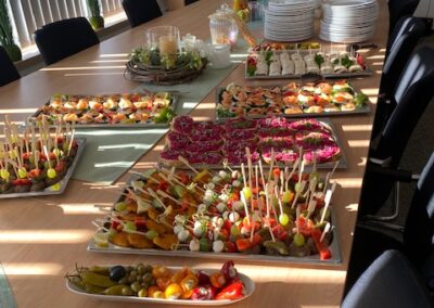 Ein gedeckter Tisch mit verschiedenen Vorspeisen, darunter belegte Brötchen und farbenfrohe Häppchen, in einem hellen Raum während eines Events.