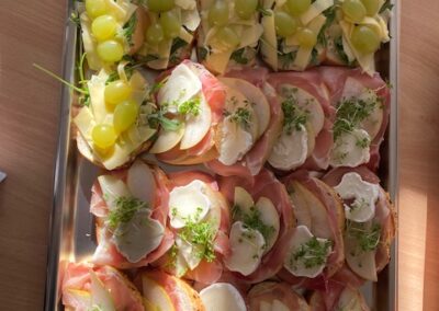 Ein Tablett mit belegten Brötchen und kleinen Snacks für die Party; oben sind Trauben und Käse, unten Schinken und Sahne-Quark.