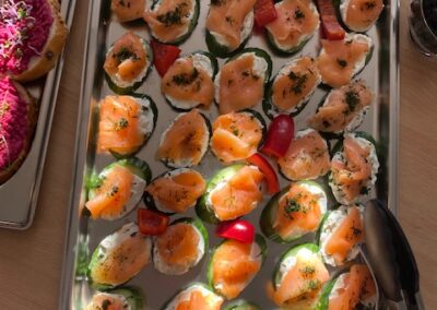 Eine große Platte mit frischem Lachs auf Gurkenscheiben, garniert mit Frischkäse, Dill und buntem Gemüse. Ein helles Ambiente betont die appetitliche Präsentation.