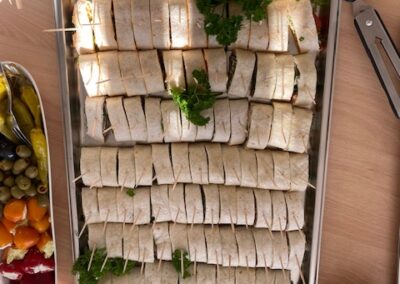 Ein großes Tablett mit aufgerollten Tortillas, gefüllt mit frischem Gemüse und garniert mit Petersilie. Die Tortillas sind gleichmäßig in kleine Stücke geschnitten.