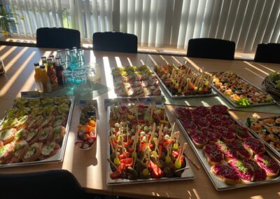 Ein reichhaltiges Buffet mit verschiedenen Snackplatten und Getränken auf einem Tisch in einem hellen Raum; die Snacks sind bunt und vielfältig angerichtet.