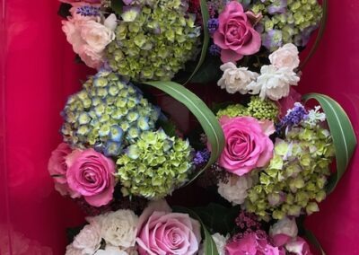 Bunte Blumenarrangements in einer pinken Box, bestehend aus Rosen, Hortensien und anderen floralen Elementen in verschiedenen Farben.