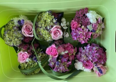 Sechs Blumensträuße aus rosa Rosen, blauen und grünen Hortensien sowie anderen bunten Blumen in einer grünen Box.