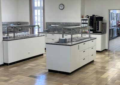 Helle, moderne Küche mit mehreren Kochinseln, weißen Wänden und glatten Böden; die Einrichtung wirkt gepflegt und funktional.