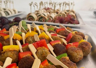 Eine Auswahl an Fingerfood mit einer Platte voller frischer Gemüsespieße und Dips sowie verschiedenen belegten Röllchen im Hintergrund für eine ansprechende Präsentation.