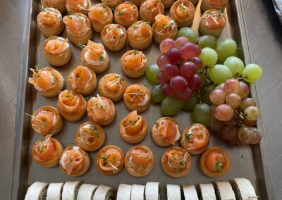 Ein Serviertablett mit verschiedenen fingerfood Snacks: Lachshäppchen auf Blätterteig, gefüllte Tortilla-Röllchen sowie Trauben in verschiedenen Farben.