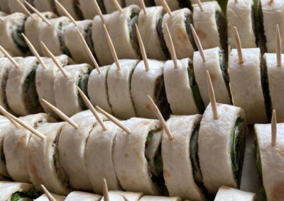 Eine große Platte mit leckeren Tortilla-Röllchen, gefüllt mit frischem Gemüse und Kräutern, auf denen kleine Spieße stecken.