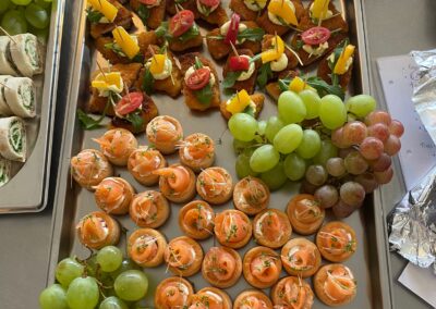Ein Tablett mit verschiedenen Fingerfood-Spezialitäten, darunter gesunde Snacks mit Trauben und Lachs. Bunte Spieße aus Gemüse, Obst und Brot sind ebenfalls vorhanden.